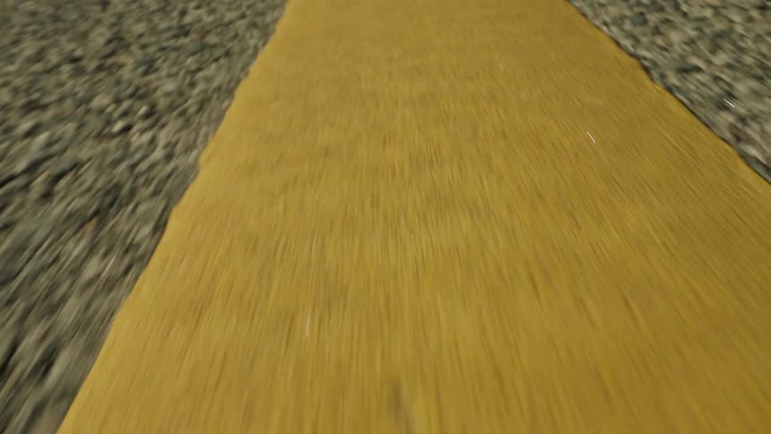 A wide yellow line is painted on the rough surface of a road