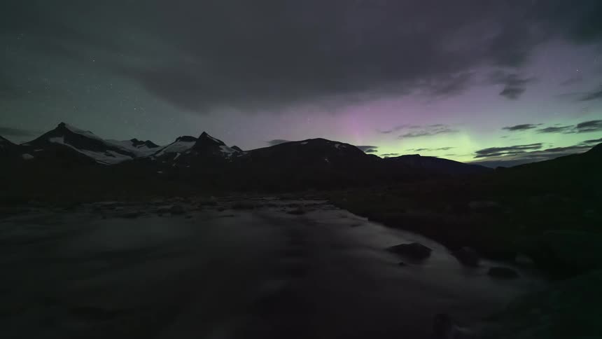 The northern lights glow over snow covered mountains and an ice covered lake