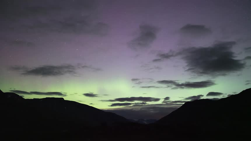 Silhouette of mountains with the sky in time lapse with black clouds and aurora borealis