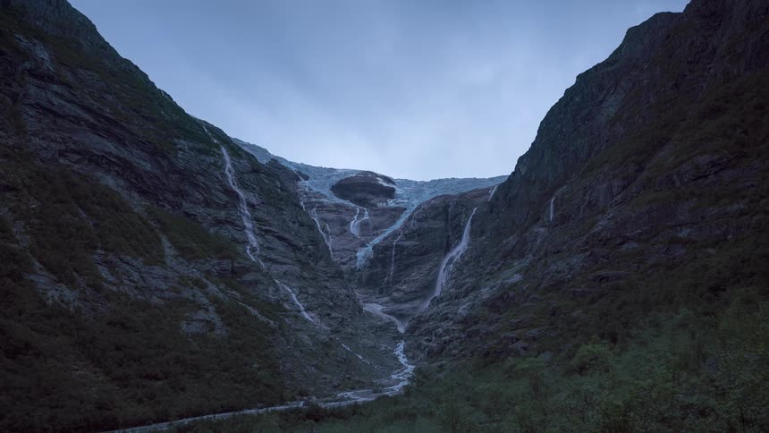 A waterfall in a mountain valley during a cloudy day
