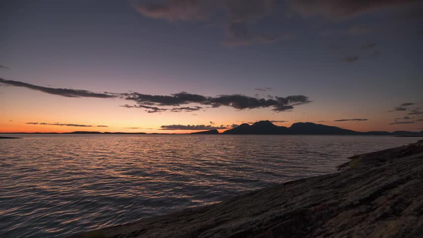 Time lapse of a golden sunset over a calm sea with distant mountains