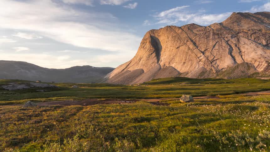 A vast grassy field with patches of water surrounded by mountains under a clear sky