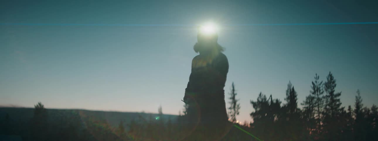 A woman in snow gear and a flashlight on her forehead in a forest at night checking a map