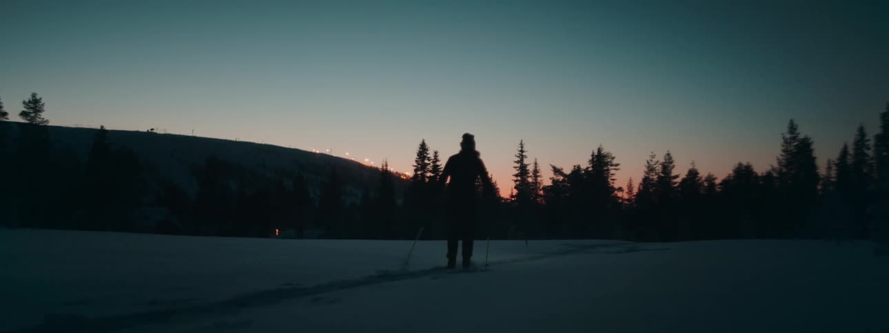 A woman cross country skis across a snow covered area