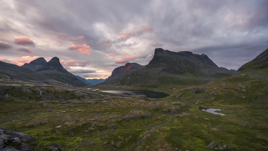 Rugged terrain with mountains and a small lake at sunset