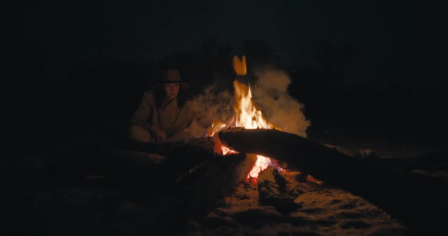 Lady sits near a madeup fire at night