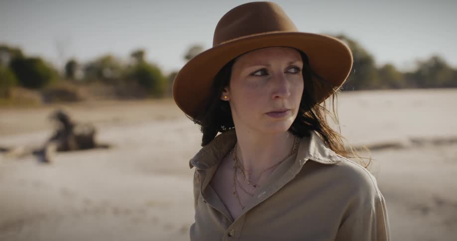 Woman with a sun hat and long hair looks around the african savanna