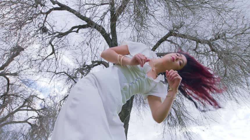 A woman dances shaking her colorful hair next to a bare tree