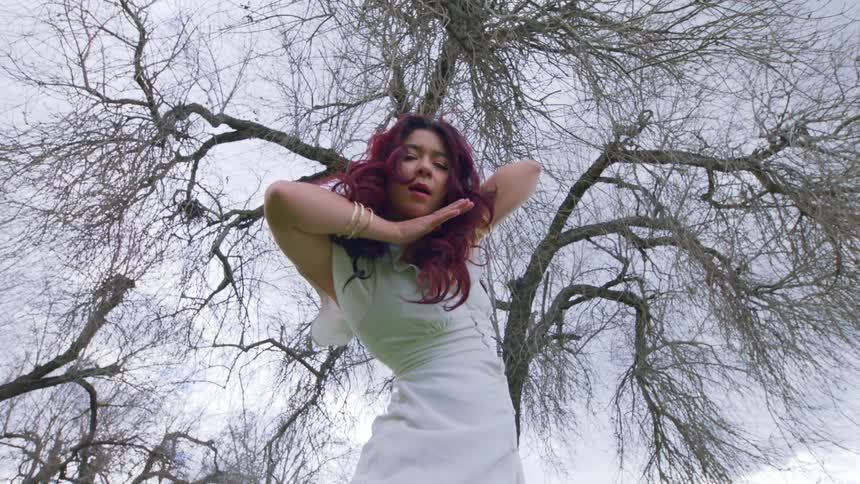 Young woman in an open environment on a cloudy day dancing gesturing her arms