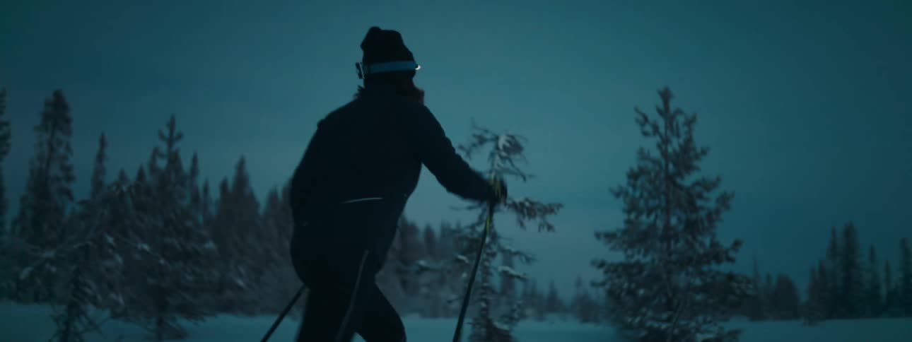 Lady walking on snow with skis and headlamp at sunset
