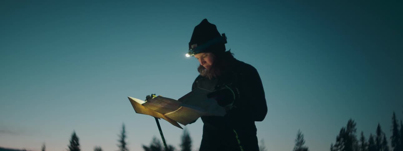 A woman stands outside wearing a headlamp as she looks at a map