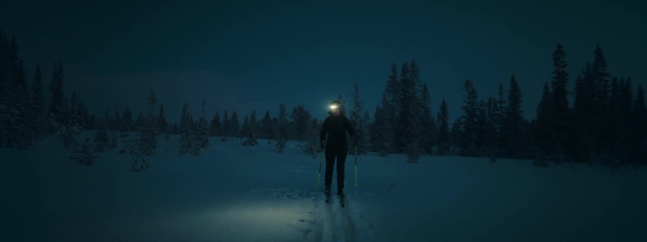Woman cross country skiing by the light of a headlamp in a wooded area