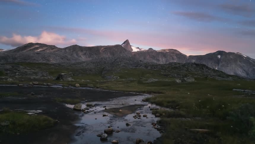 A small stream in a field surrounded by mountains during dusk