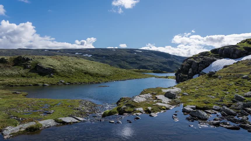 Icelandic landscape with green moss white ice gray rocks and small lakes that reflect the blue sky and rolling white clouds