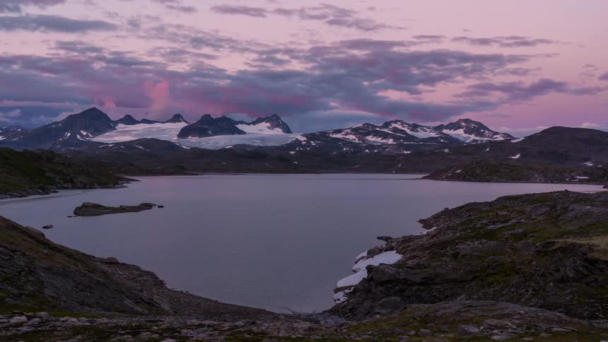 Landscape of mountains covered in snow around a lake with a darkening day in timelapse