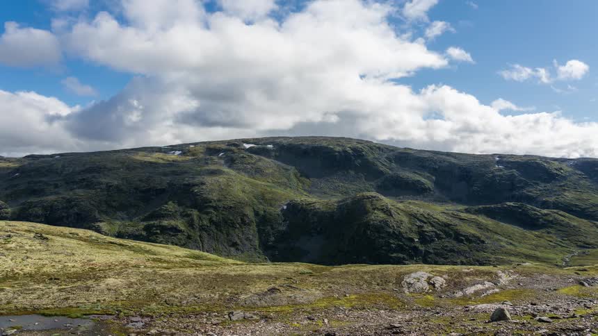 Time lapse of rolling white clouds over green hills