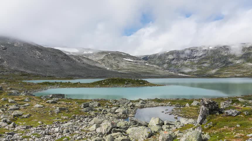 Clouds move over a lake surround by highlands covered in moss and loose rocks during the day