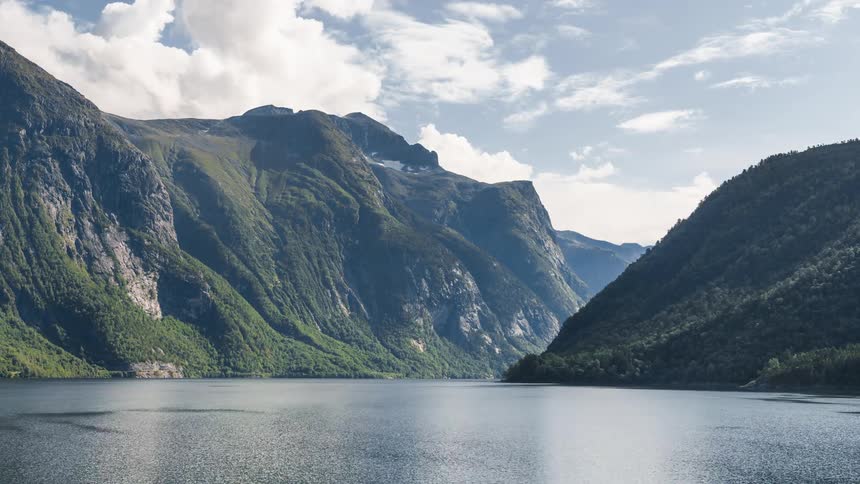 A serene lake surrounded by green mountains under a partly cloudy sky