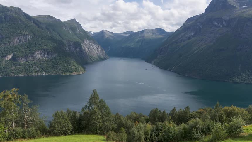 A vast lake surrounded by towering mountains with lush greenery and small buildings in the foreground