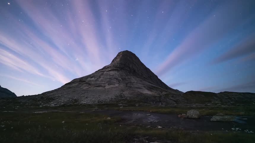 Landscape of a flowing river with a rocky mountain and clouds passing through the sky in timelapse