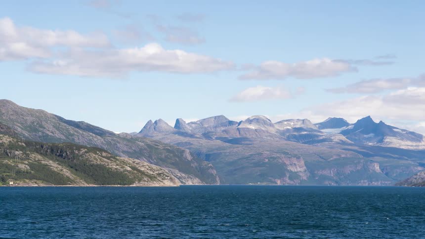 Landscape of mountain range by the blue sea on a clear day with few clouds