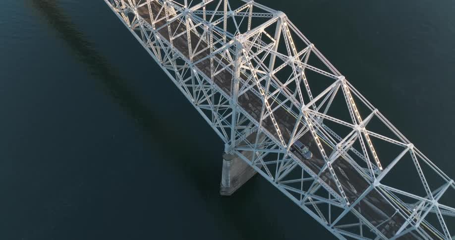 A car drives along a bridge deck as sunshine glows on the steel beams