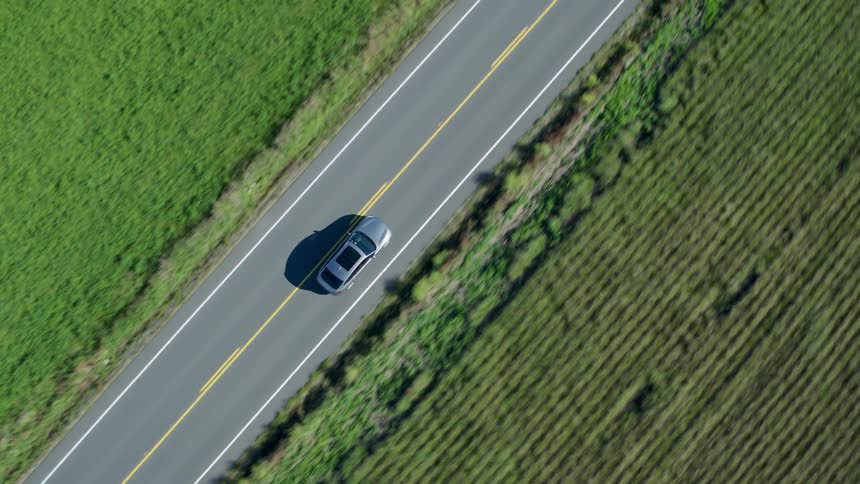 Twisting birds eye view of gray sports car driving on a two lane highway between farm fields