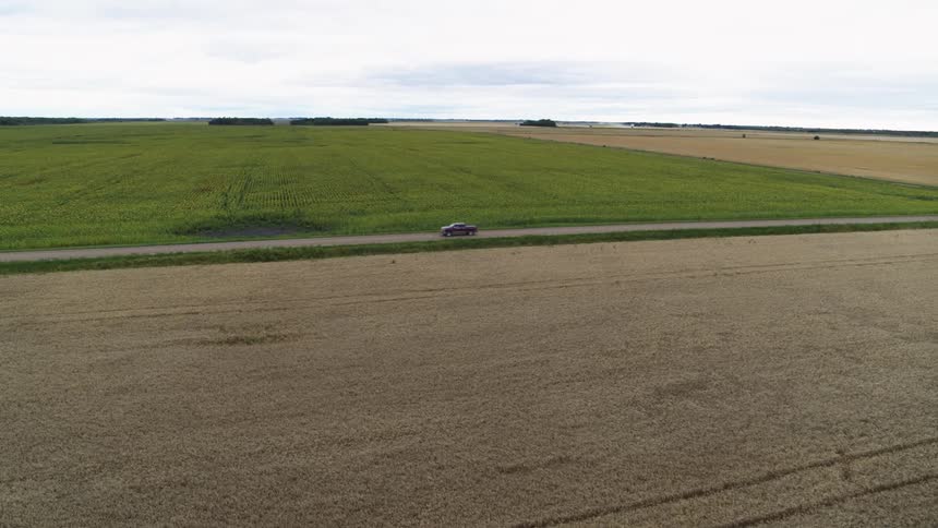 Ascendiing over crop fields as a dark red pickup drives along a rural county road