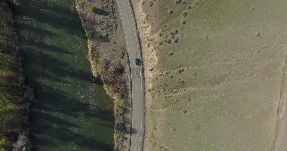 A car drives on a curved two lane highway between a steep hillside and rushing river