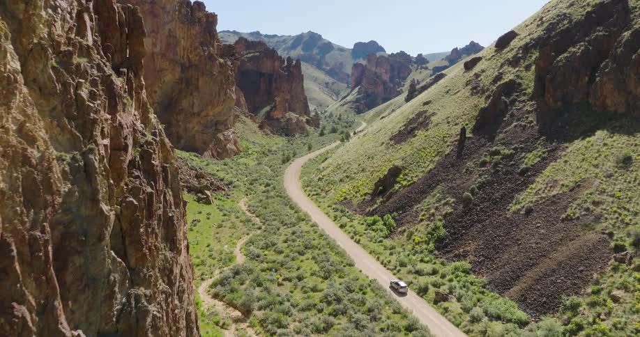 A car travels along a winding road in the valley of a spectacular canyon
