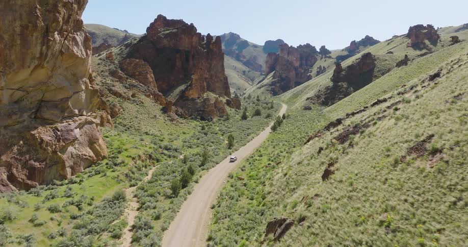 A car drives on a gravel road through incredible hills and rock formations