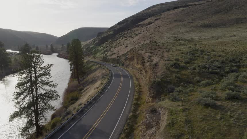 A SUV tows a trailer with a fishing boat down a curved highway next to a river