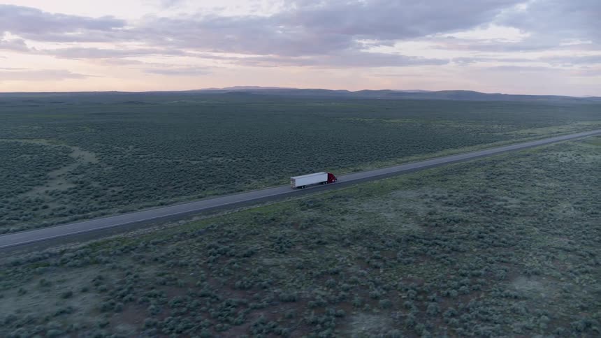 A red and white semi truck drives along open highway under a painted sky