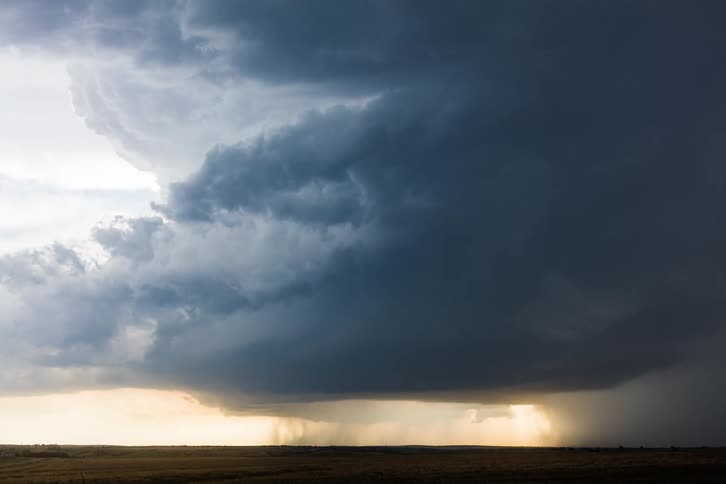 Sunrays shine behind twisting dark thunderstorm clouds over grassy prairie