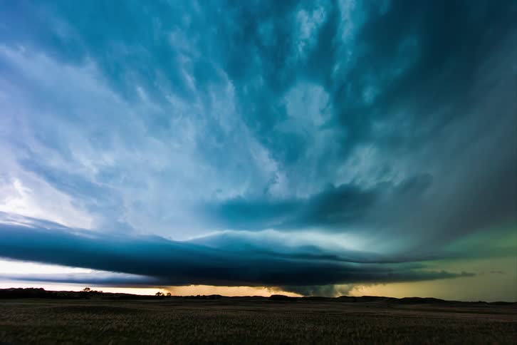 Lightening rapidly flashing in sky filled with swirling blue clouds over a grassy plain