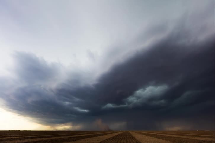 Thunderstorm clouds rolling over rows of planted farmland