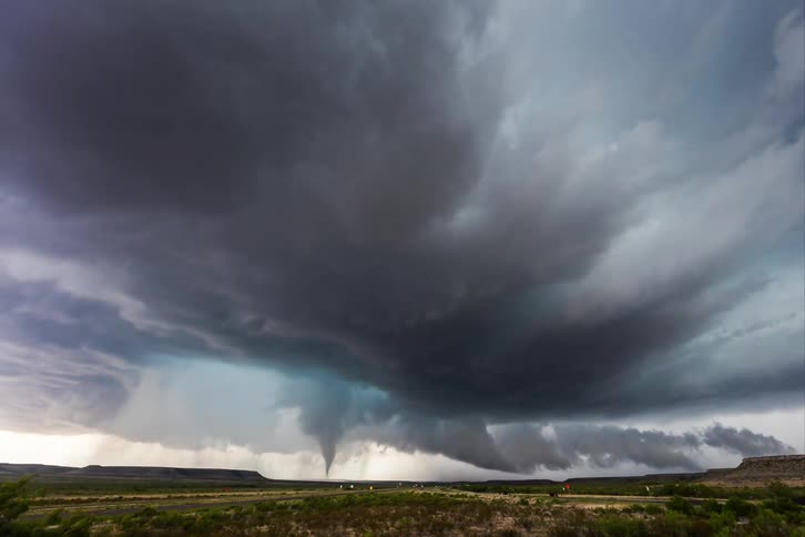 A tornado funnel cloud moves over farmland as traffic flows and stops on the road