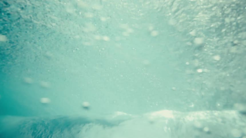 A cameraman submerges under a wave in the ocean