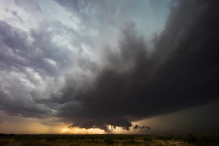 Storm clouds move across the sky as lightning flashes and sunlight glows on the horizon