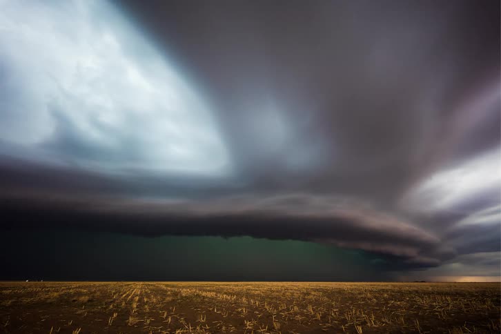 Dark storm clouds and a supercell storm move over the land as lightning flashes and strikes the ground