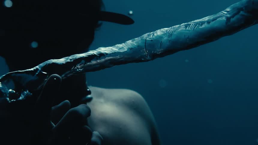 A man underwater breaks a rising bubble with his finger