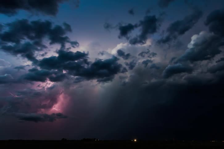 Storm clouds move across the sky as lightning flashes and illuminates the darkness