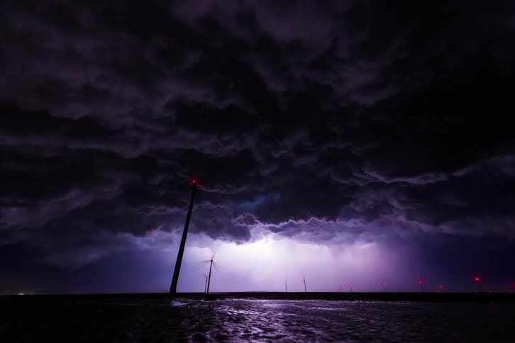 A stormy night at sea with lightning illuminating the clouds and wind turbines