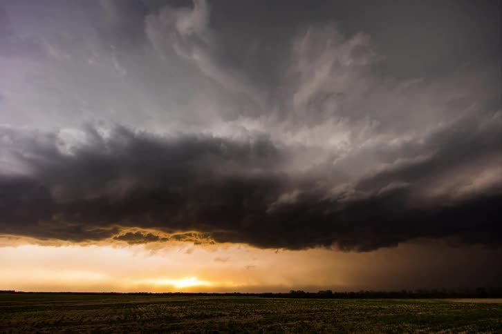 Dark storm clouds move across the sky as the sun glows on the horizon