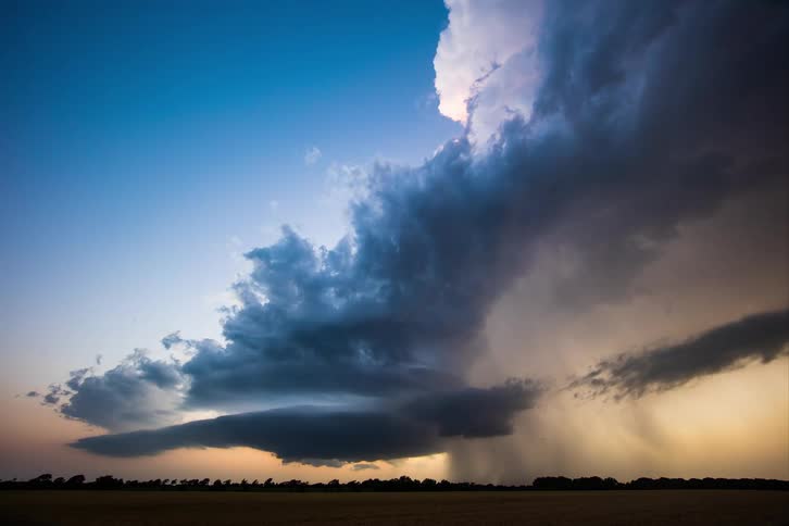 Dark clouds pour rain on rural land as the sun glows on the horizon