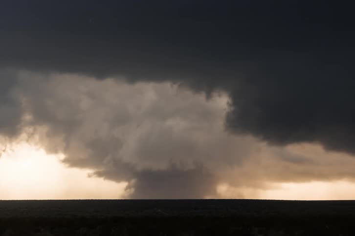 Black clouds spun into a tornado moving across grassy farmland