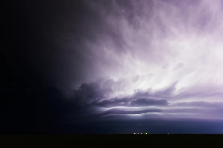 Lightening illuminates clouds in a black sky over a highway at night