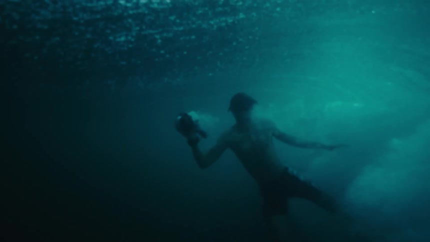 Man swims under the sea wave holding a camera at midday