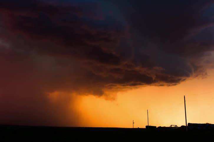 A dark storm cloud is in rotation near the ground as it pours down rain and lightning strikes