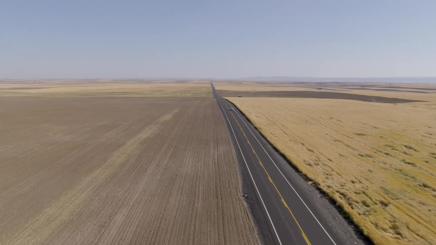 Subtle orbit around a car driving down a road that stretches to the horizon between wheat fields